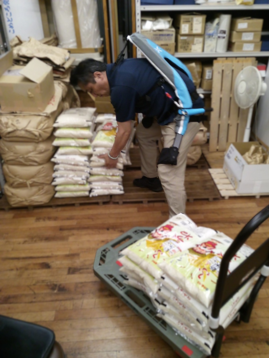 ごとう米店の倉庫内でマッスルスーツ Exo-Powerを着用し30kgの米袋を持ち上げる作業風景